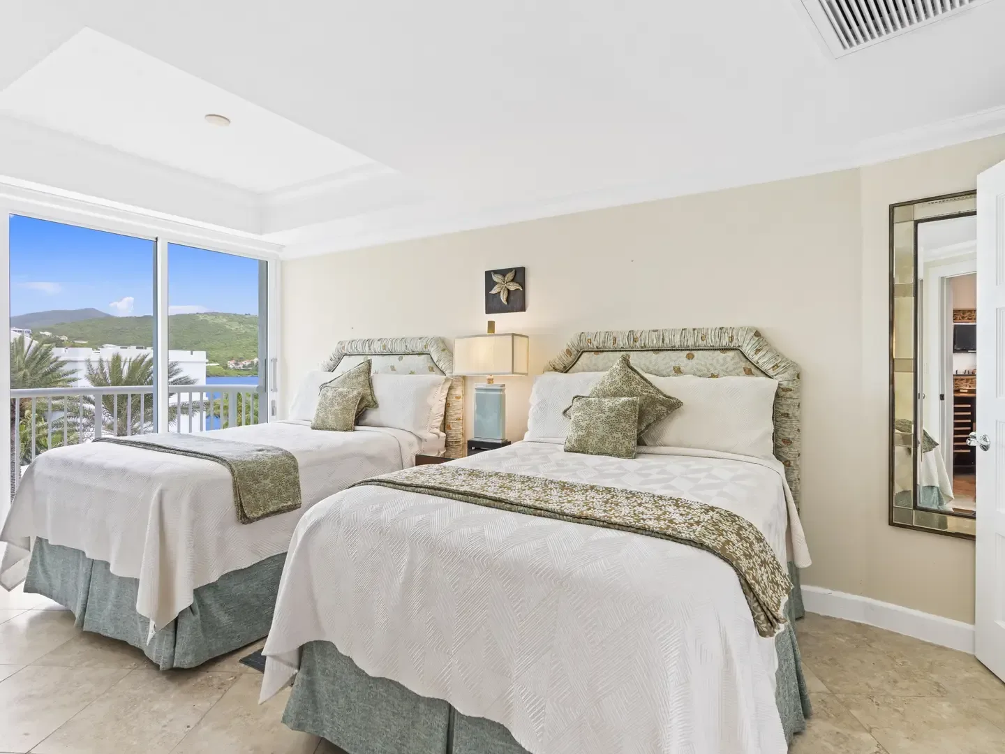 Bright bedroom with two twin beds, white linens, ocean and hill views through sliding glass doors, coastal decor