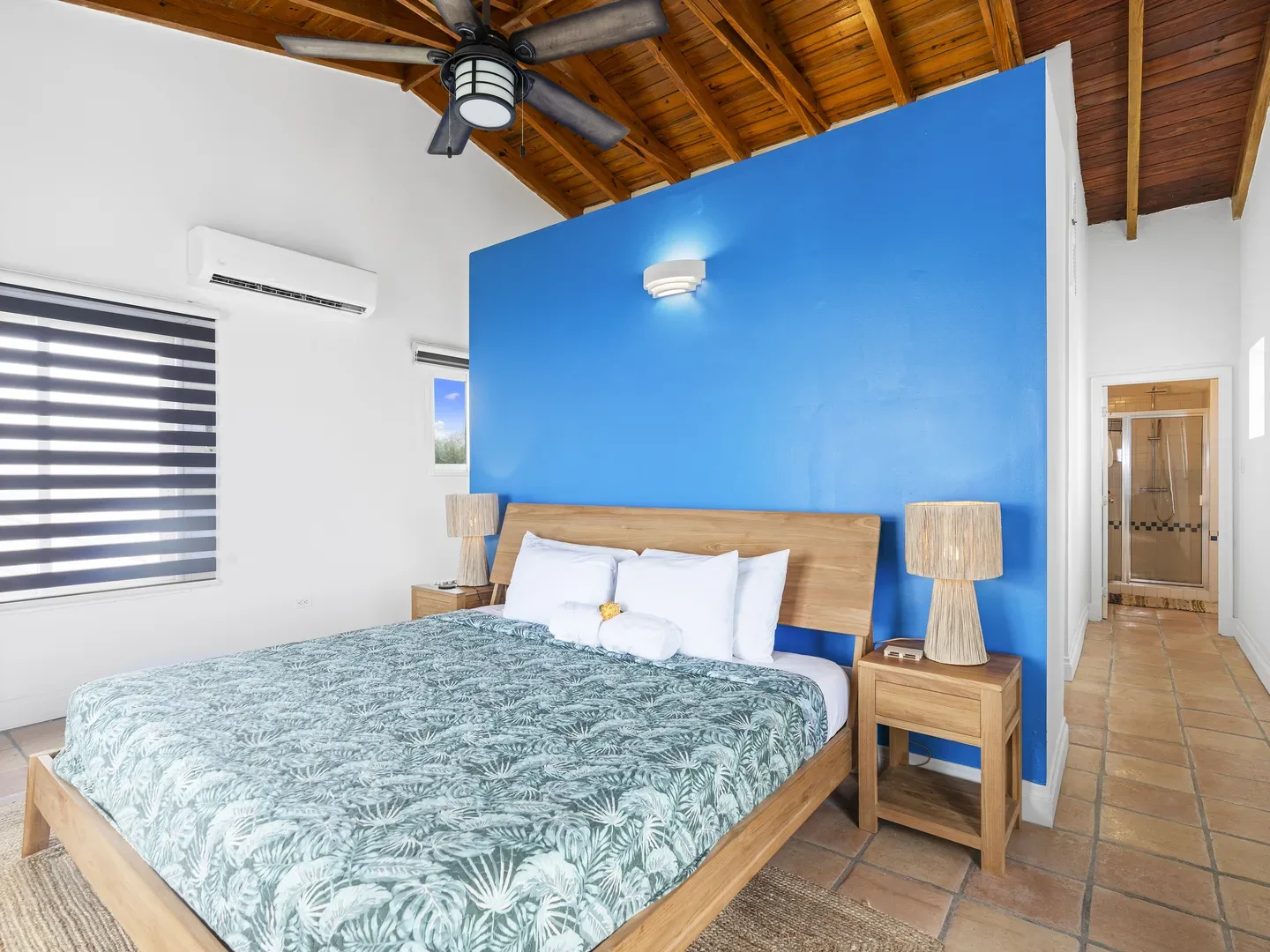 Spacious bedroom with large bed, blue accent wall, wooden nightstands, wicker lamps, and view of en-suite bathroom