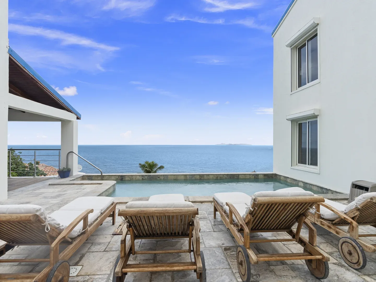 Villa terrace with wooden lounge chairs, infinity pool, and panoramic ocean view