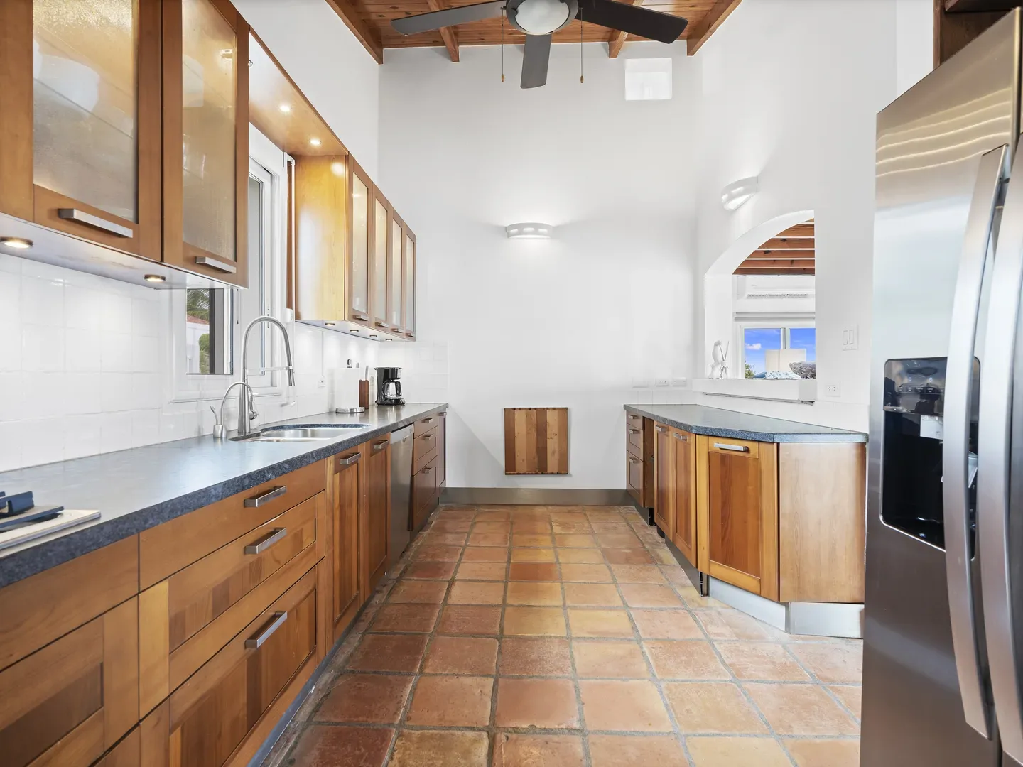 Modern kitchen with wooden cabinets, stainless steel refrigerator, terracotta tile flooring, and ocean view through window