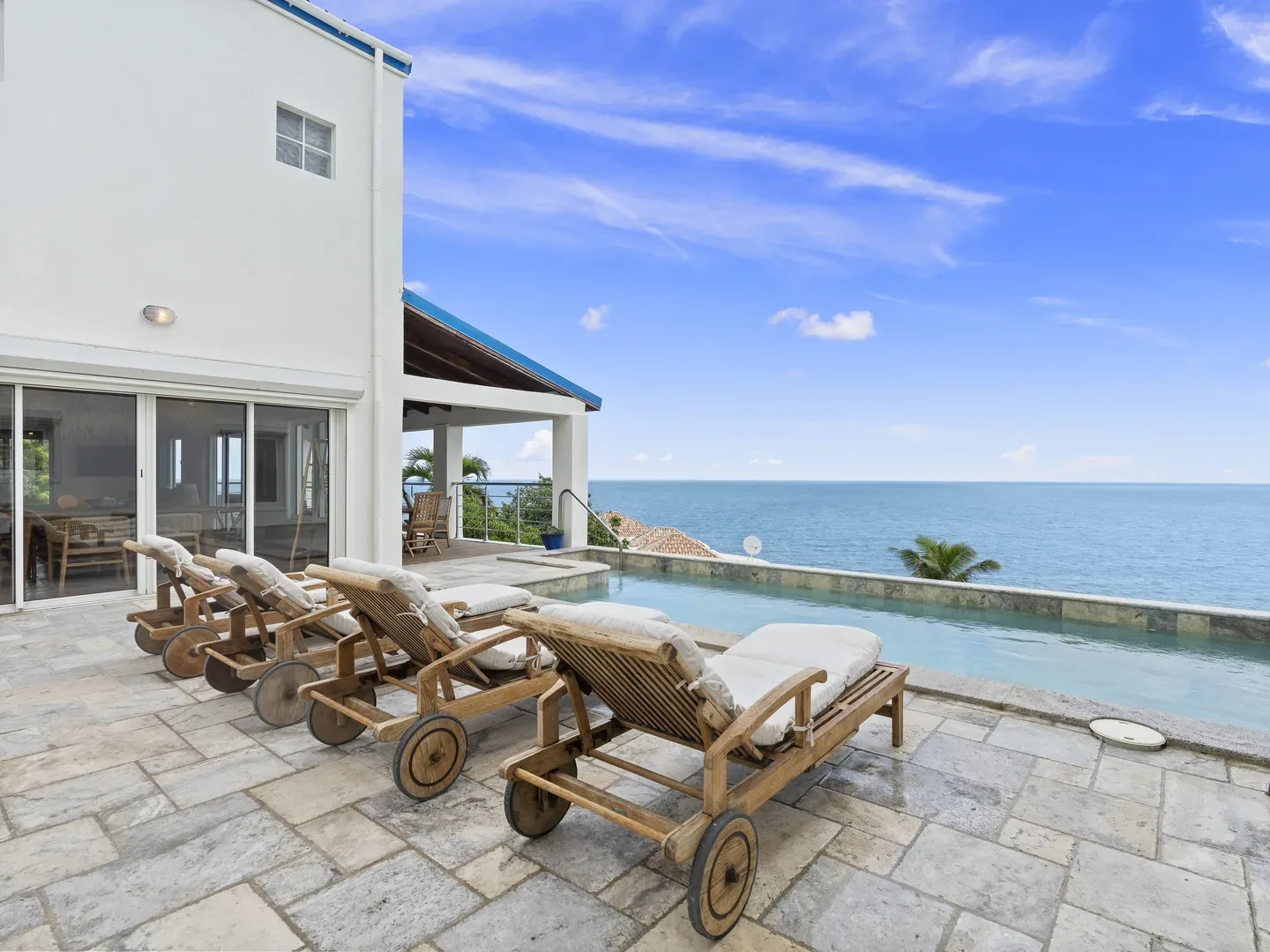 Villa patio with wooden wheelbarrow lounge chairs, swimming pool, and ocean view under bright blue sky