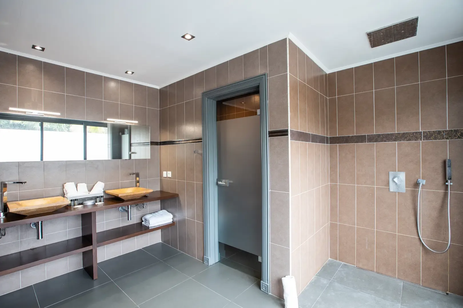 Modern simplicity defines this bathroom with walk-in rain shower, dual vessel sinks on wooden vanity, and large-format neutral tiling.