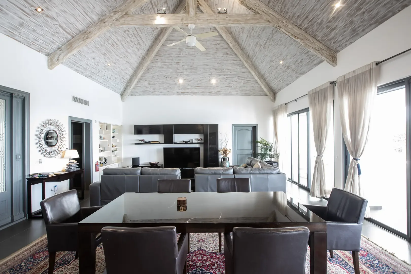 Entertain in style under soaring wood-beamed ceilings, where a dark wood dining set for six meets a spacious grey leather sectional and ornate area rug.
