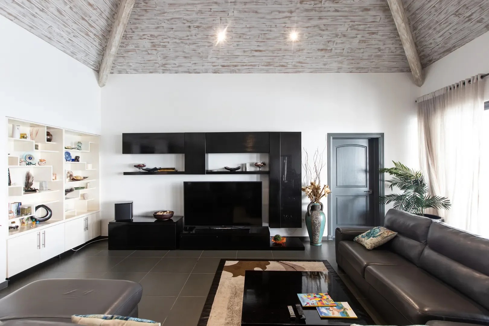 High vaulted whitewashed wood ceilings crown this modern living space, where a leather sofa faces a sleek black media unit with flat-screen TV and built-in display shelving.