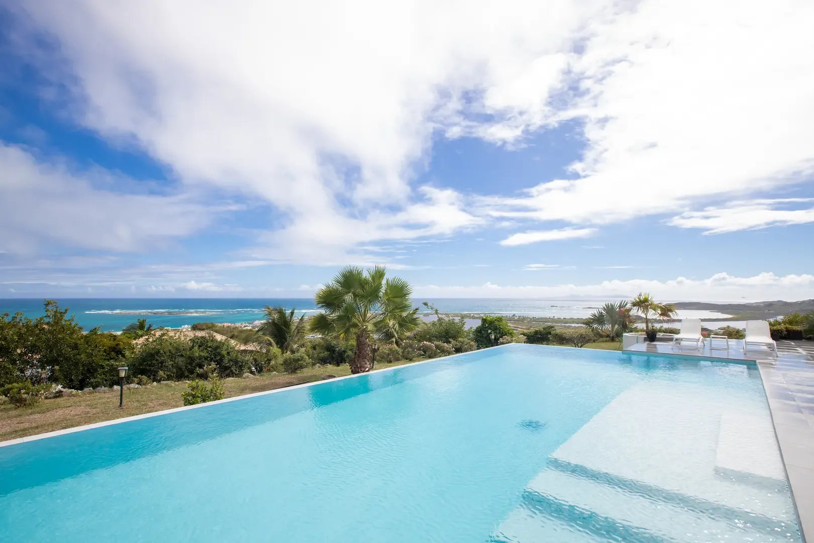 Your private infinity pool stretches toward the horizon, where crystal-clear water meets panoramic views of Orient Bay and the Caribbean coastline under swaying palms.