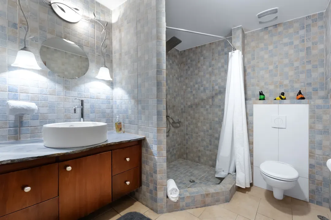A bathroom with Caribbean flair — mosaic tiles, a curved light fixture, and a walk-in shower for effortless relaxation.