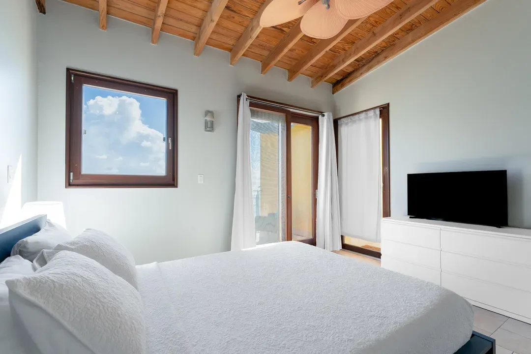 Tropical charm meets modern comfort — exposed wooden beams, a plush bed, and natural light flooding through sliding doors.