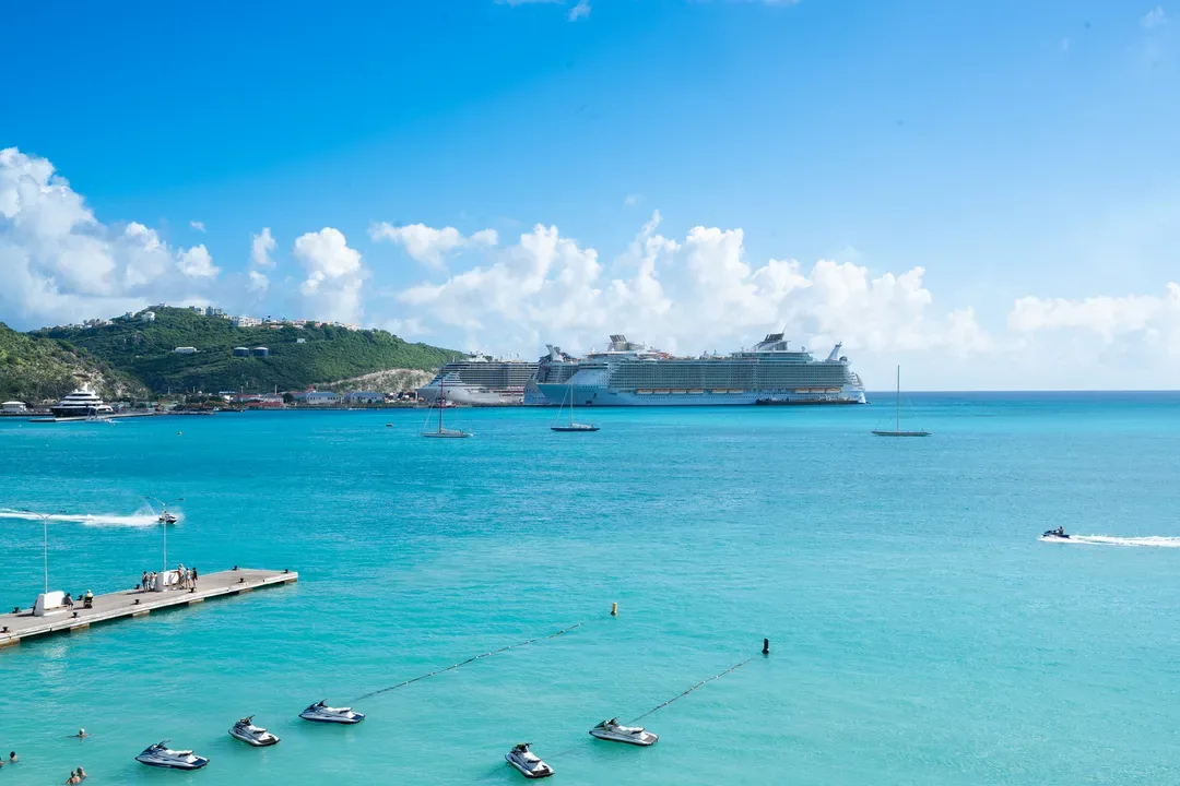 The ultimate Caribbean view — a pier lined with jet skis, sailboats dancing on turquoise waters, and a majestic cruise ship at anchor.