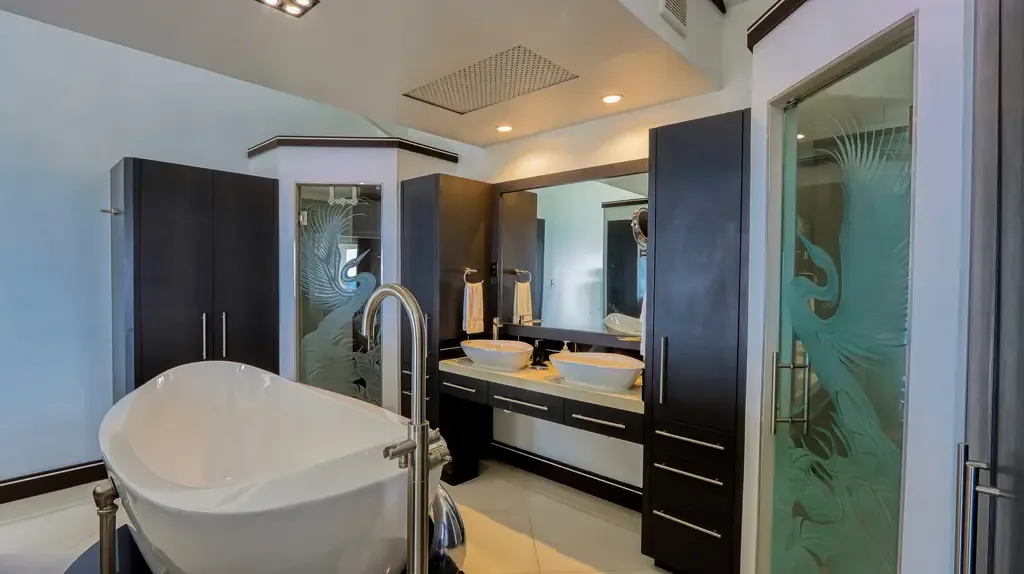 A luxurious master bathroom features a large freestanding white tub, double vessel sinks on dark cabinetry, and elegant frosted glass shower doors with decorative bird designs.
