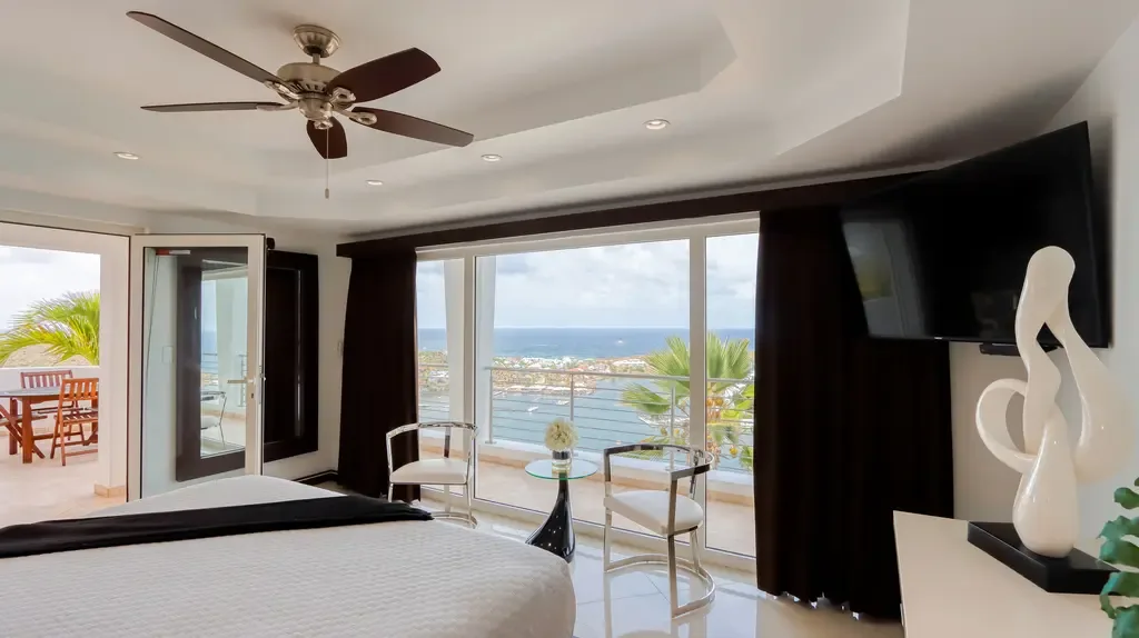 Floor-to-ceiling windows capture a stunning ocean and harbor view in this luxurious modern bedroom with sleek seating area.