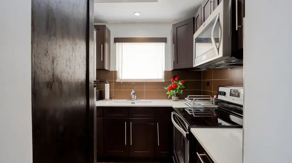 The modern kitchen showcases dark brown cabinetry, white countertops, stainless steel appliances, and a small vase of red roses as decor.