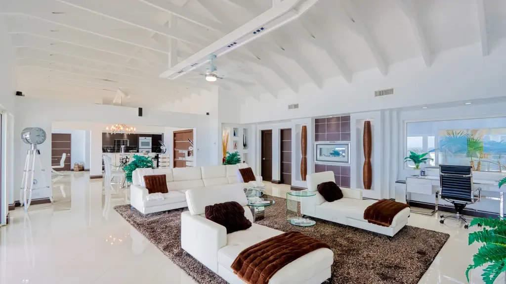 High vaulted beamed ceilings crown this spacious living area with white leather seating, a large shag rug, and a modern home office nook.
