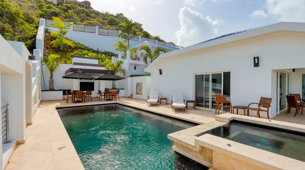 A spacious outdoor pool area includes a large swimming pool, adjacent hot tub, several lounge chairs, and outdoor dining sets against a white modern villa backdrop.