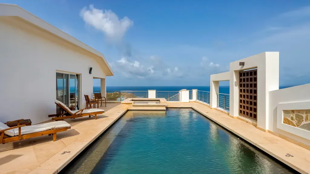 The luxurious rooftop infinity-edge pool area features lounge chairs, a separate hot tub, and stunning panoramic ocean views under clear blue skies.