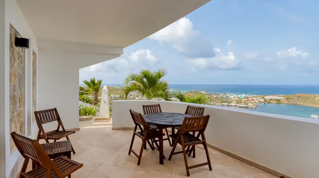 A spacious outdoor terrace features a wooden dining set for four and stunning panoramic views of the coastline and bay.