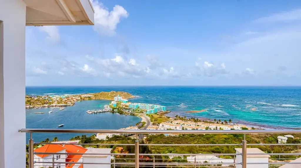 A breathtaking panoramic view from the terrace overlooks a turquoise bay, coastal buildings, and the ocean under a clear sky.