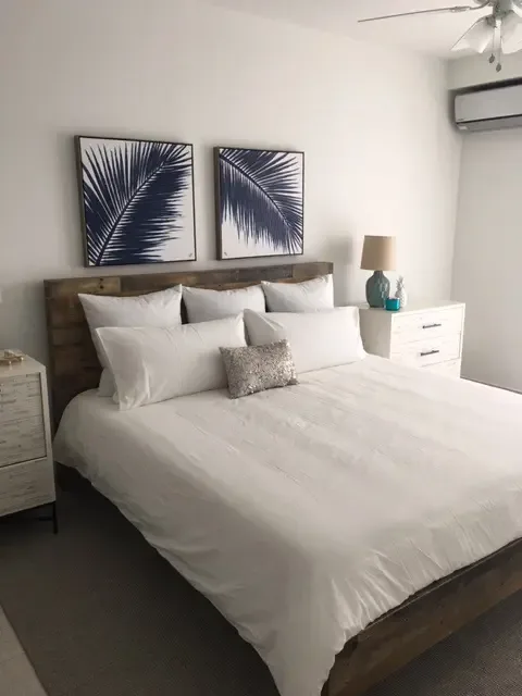 Wake up refreshed in this serene master bedroom with crisp white linens and calming palm artwork — your island retreat starts here.