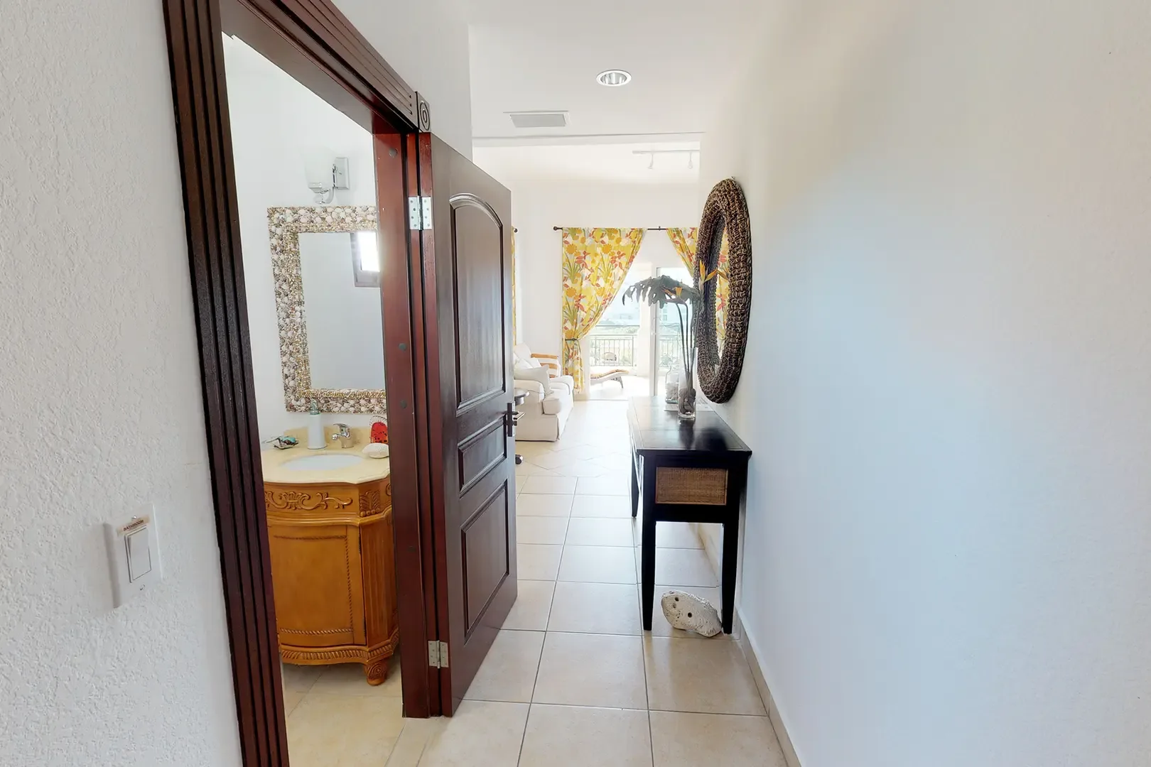 View through hallway showing ornate vanity, living area with white sofa and floral curtains, console table and round mirror.