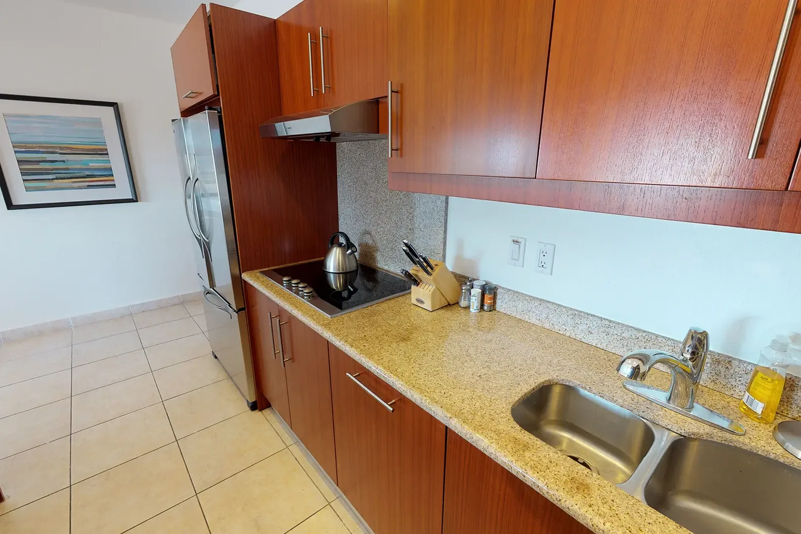 Wood cabinetry and granite countertops frame the stainless steel sink and stovetop, perfect for preparing island meals.