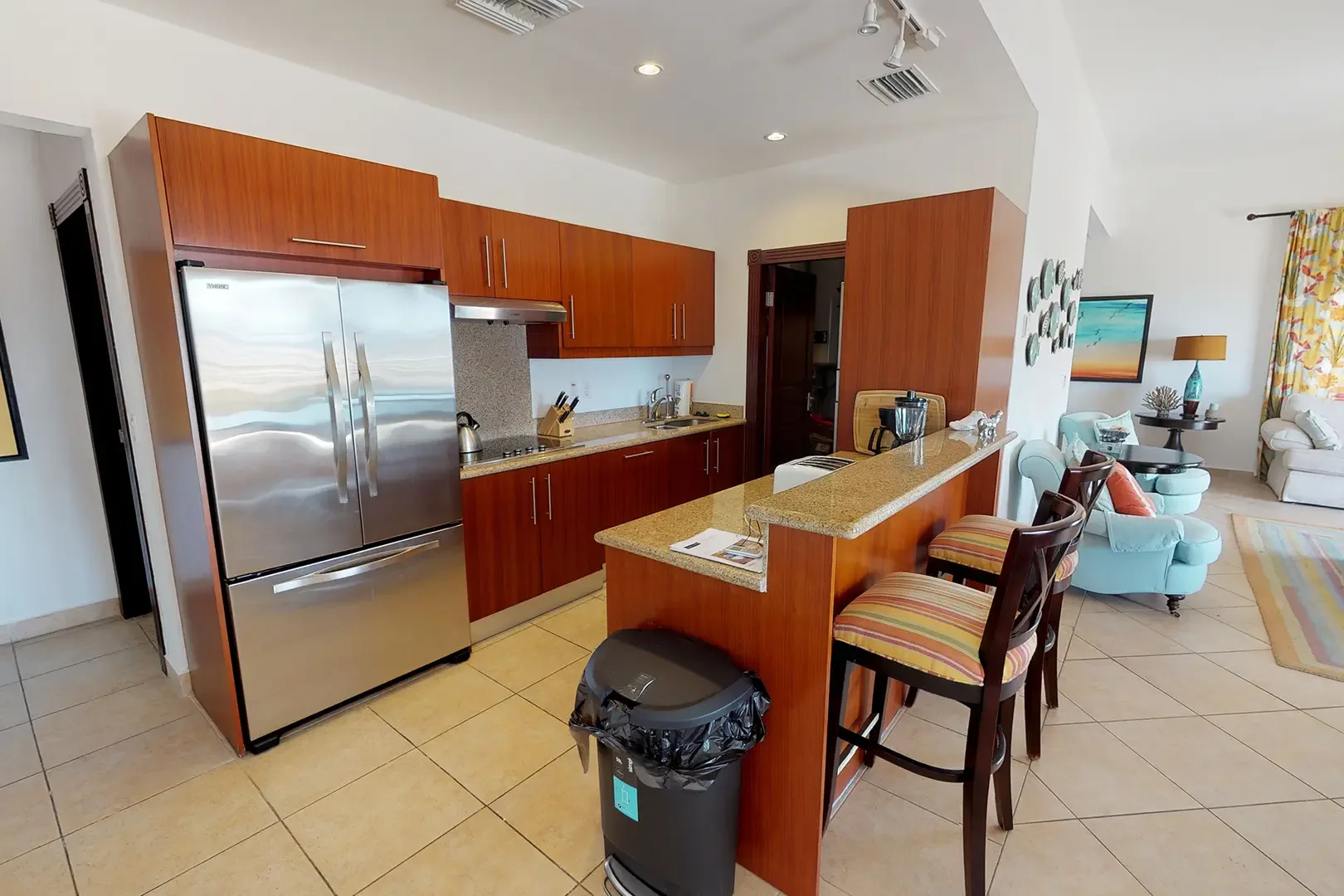 The modern kitchen showcases rich wood cabinetry, stainless steel appliances, granite countertops, and breakfast bar with striped stools overlooking the living space.