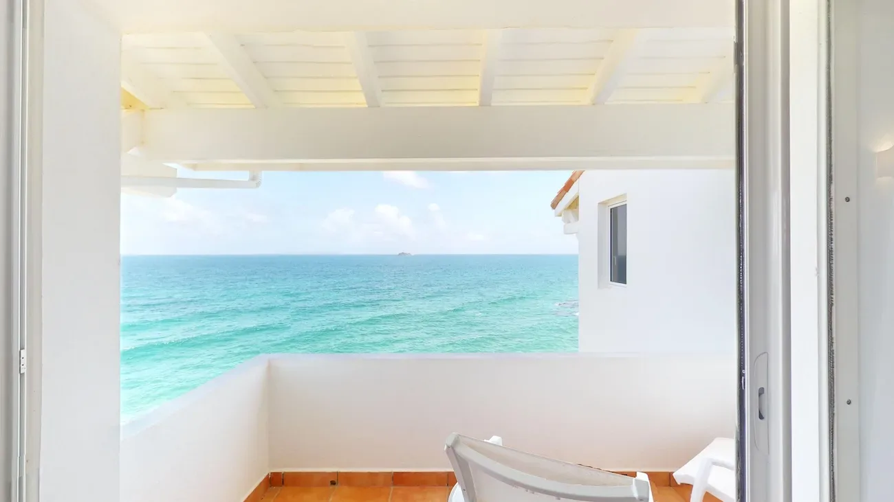 White lounge chair on a villa balcony overlooking turquoise ocean and clear sky