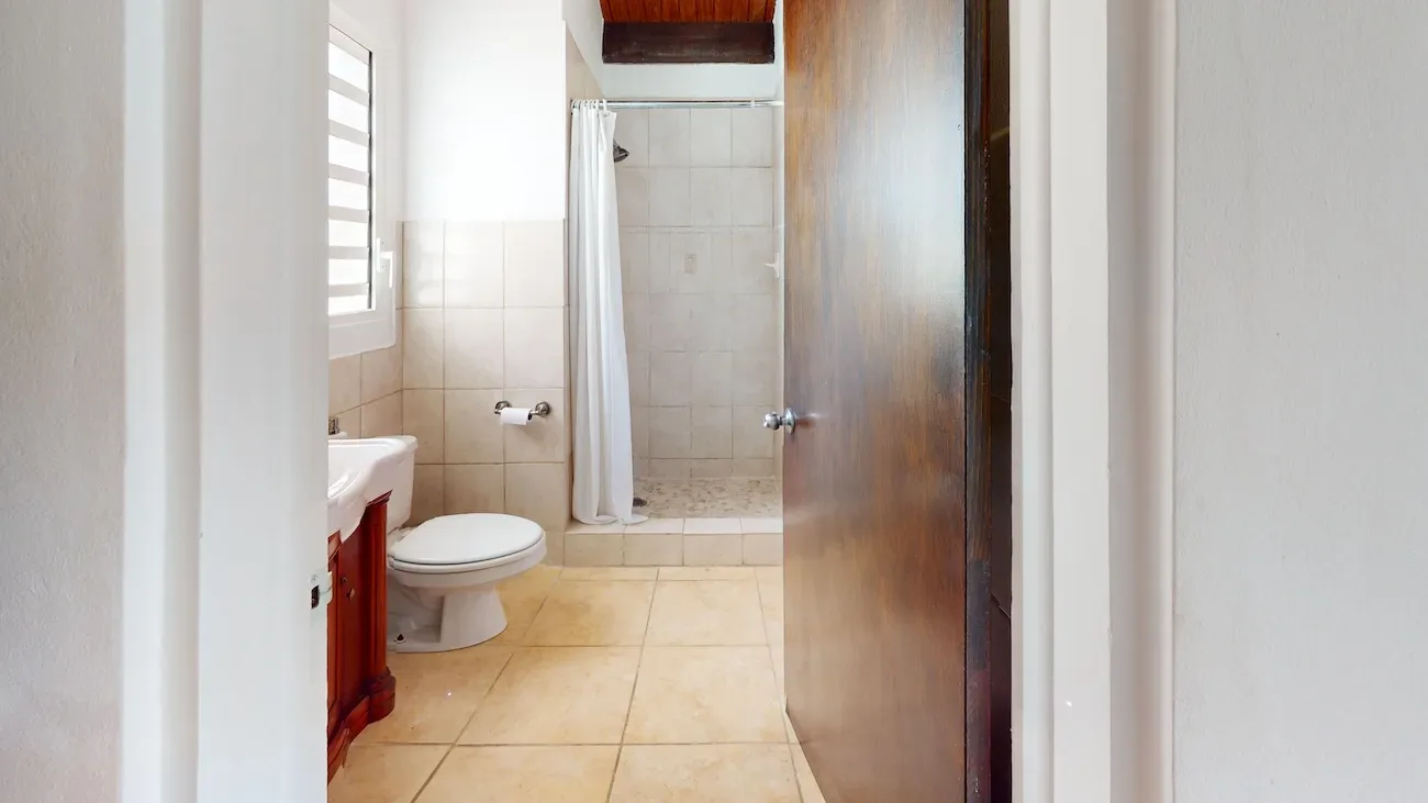 Clean bathroom with beige tile flooring, white toilet, sink with dark wood cabinet, shower area with white curtain
