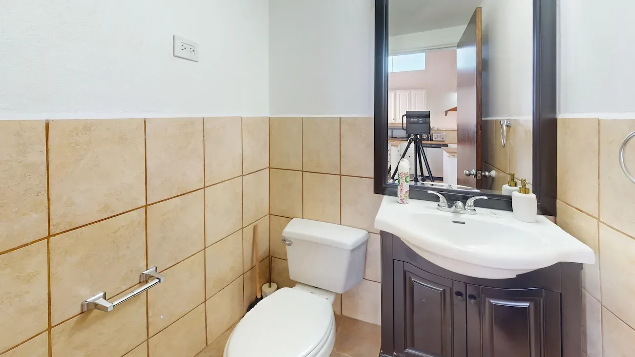 Bathroom with beige tile walls, white toilet, dark brown vanity, white sink, and large mirror