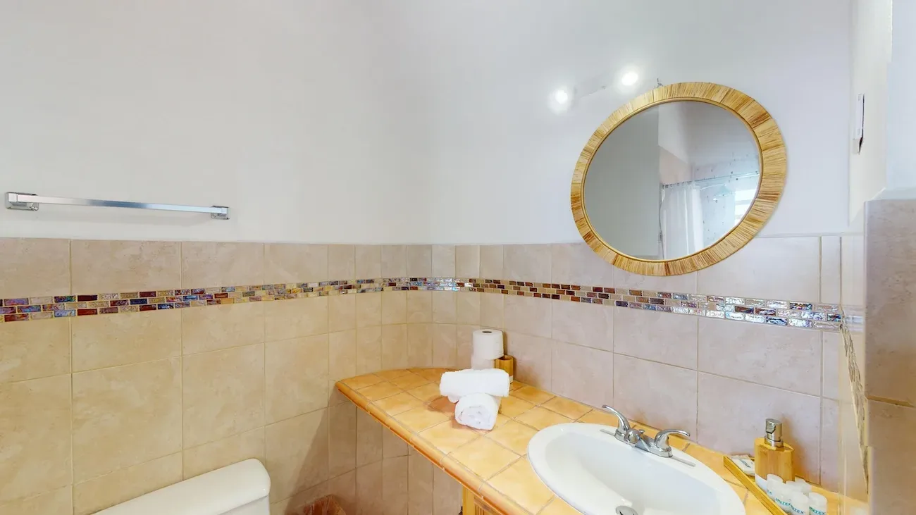 Clean bathroom with beige tile walls, round wooden-framed mirror, white sink, and yellow-tiled countertop