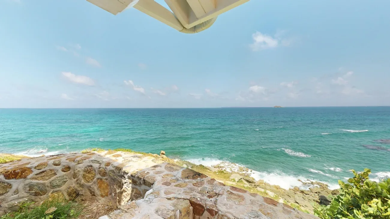 Ocean view from a stone terrace with turquoise waters, blue sky, and distant island