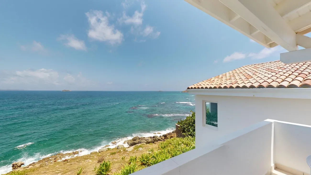 Villa terrace with white railings, terracotta roof, and turquoise ocean view from elevated coastal property