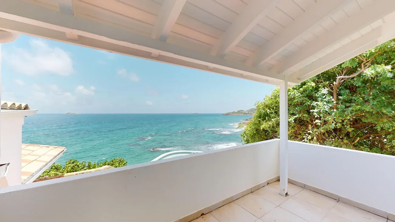 White covered balcony with beige tile flooring overlooking turquoise ocean, distant islands, and lush greenery