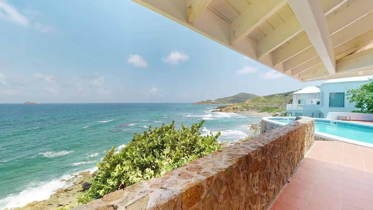 Villa terrace with stone wall, infinity pool, and turquoise ocean view against coastal landscape