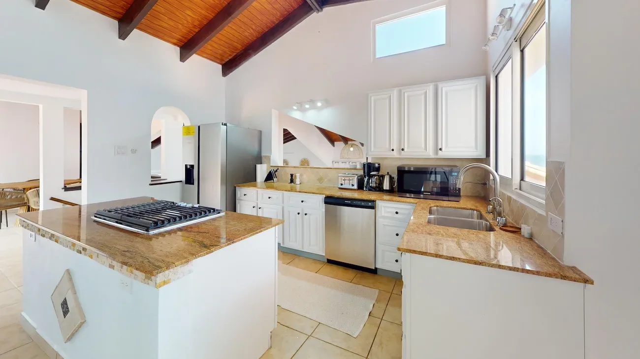 Modern villa kitchen with white cabinets, granite countertops, stainless steel appliances, and ocean view