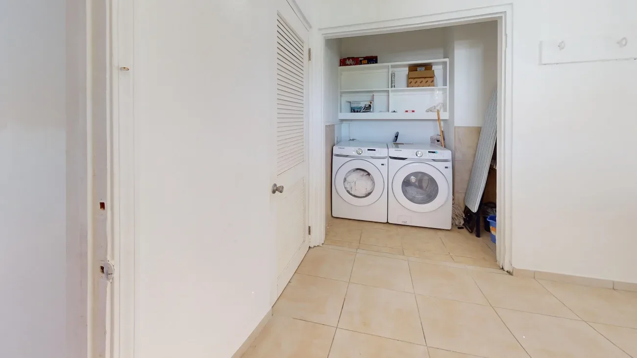 Clean laundry room with two white front-loading washing machines, shelving, and beige tile flooring