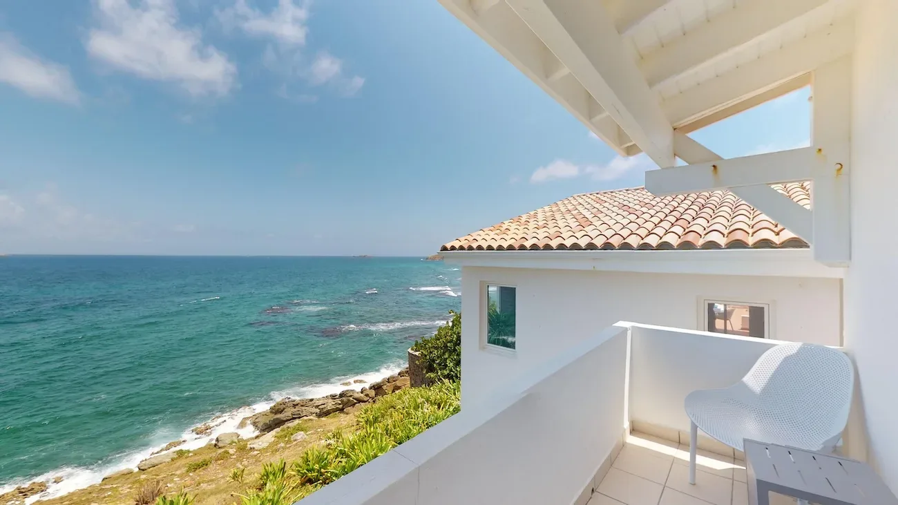 White villa balcony with chair and table overlooking turquoise ocean and rocky coastline