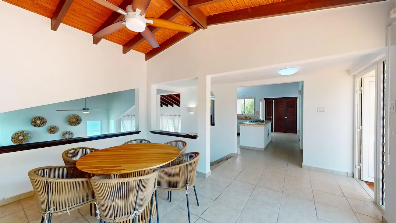 Open-concept dining area with round wooden table, wicker chairs, and kitchen view