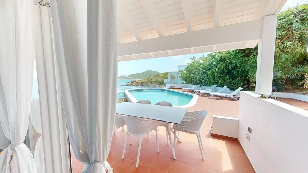 Villa terrace with white dining set, swimming pool, and ocean view