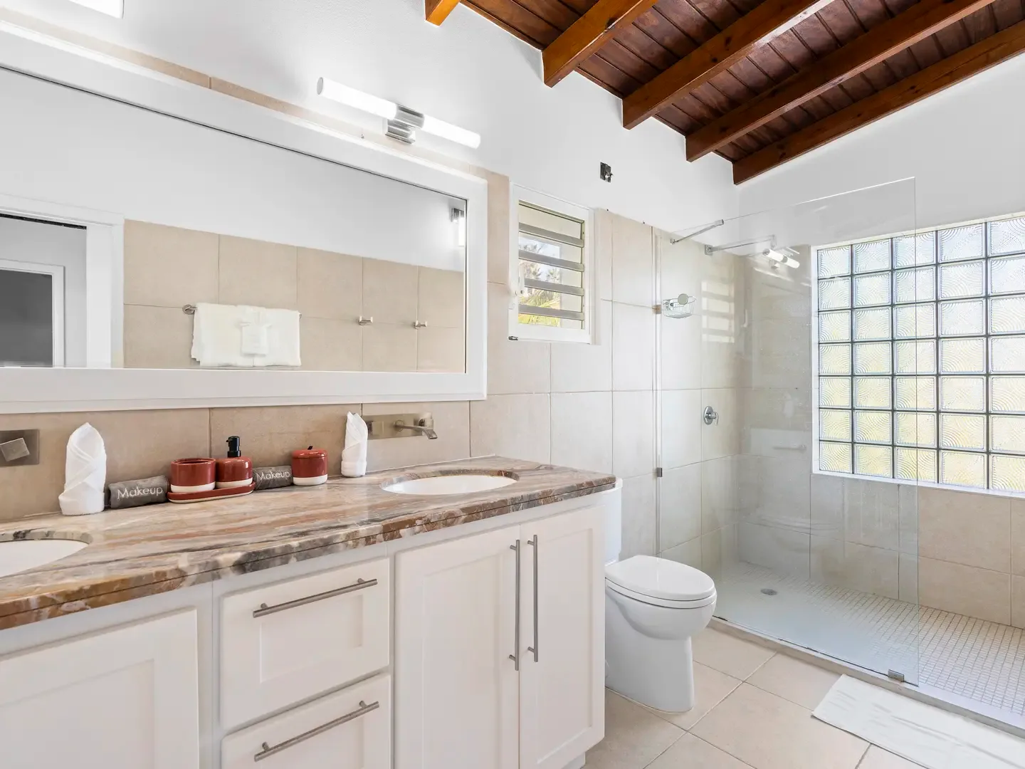 Glass-enclosed shower with premium finishes — where practical design meets the warmth of exposed wood beam ceilings.