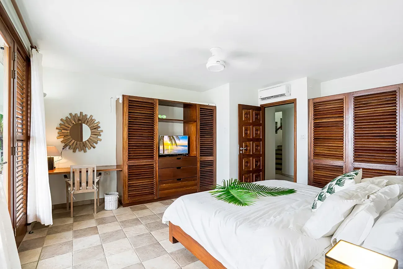 Bedroom with white bedding, wooden furniture, TV in wardrobe, desk area, and outdoor greenery view