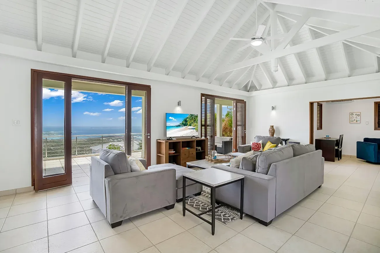 Spacious living room with gray sofas, white vaulted ceiling, and ocean view through large sliding glass doors