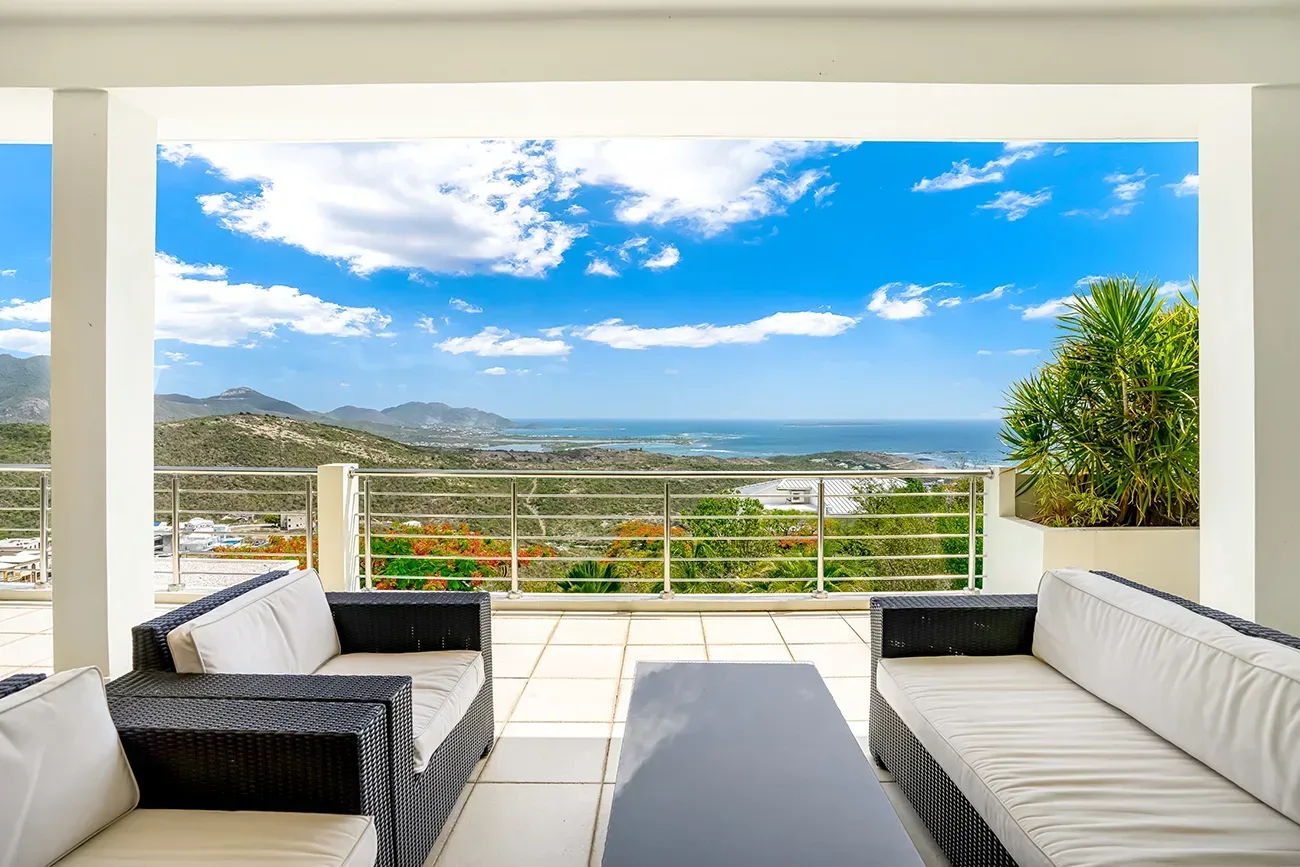 Villa terrace with dark wicker furniture, white cushions, and panoramic ocean and mountain view