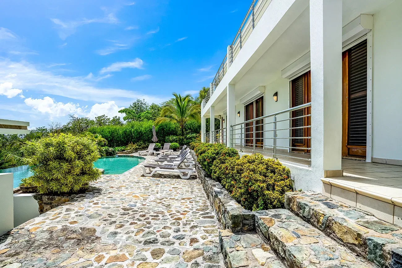 Modern villa with white exterior, private turquoise pool, stone pathway, white lounge chairs, and tropical greenery