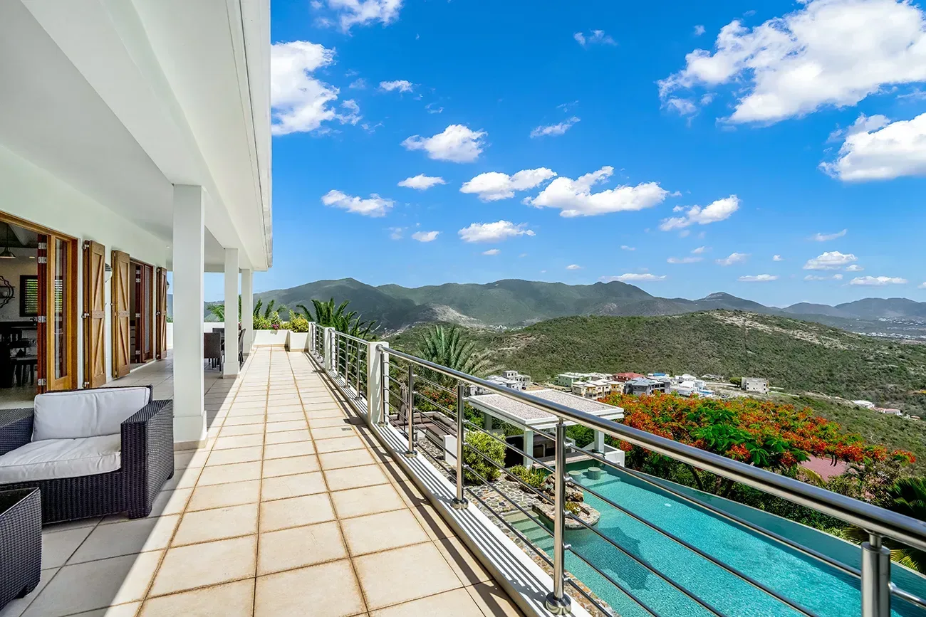 Villa terrace with wicker chairs, infinity pool, and mountain views under blue sky