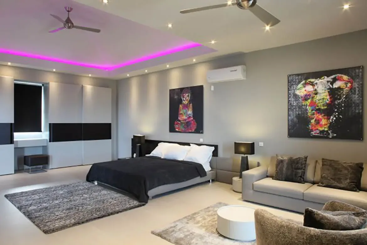 A modern suite features purple LED cove lighting, large black bed, grey seating area, and vibrant contemporary artwork.