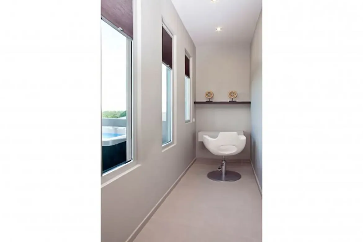 A narrow hallway or study area features vertical windows overlooking the pool, built-in white desk, modern white swivel chair, and decorative shelf.