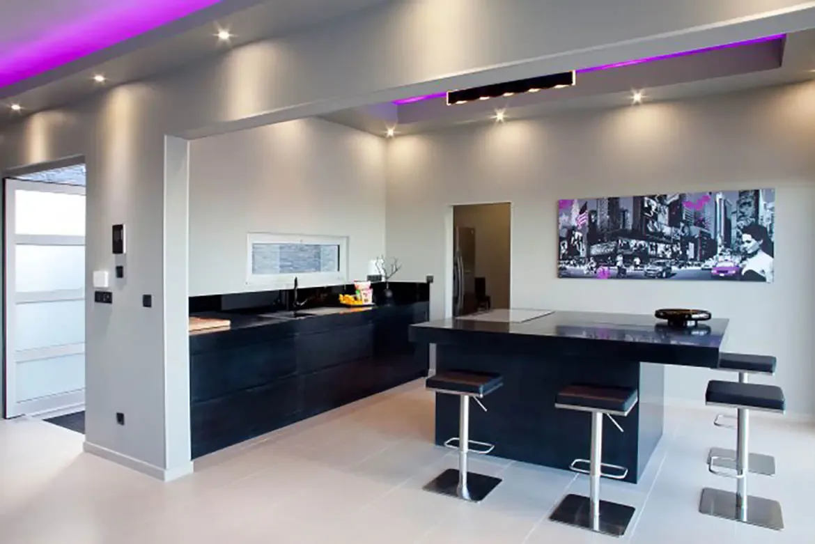The modern kitchen showcases black cabinetry and island with purple cove lighting, and a large black-and-white city skyline artwork.