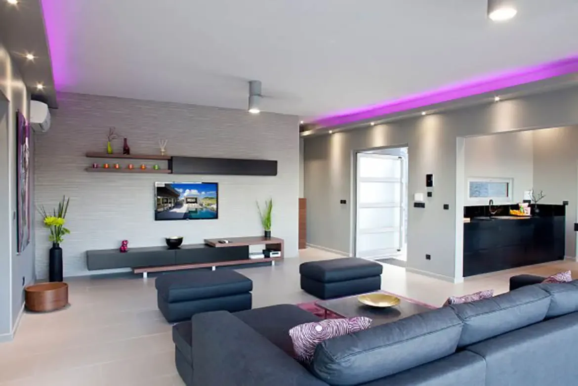A modern open-plan living area showcases minimalist aesthetic with grey tones, textured feature wall, vibrant pink LED cove lighting, sectional sofa, and sleek media console.