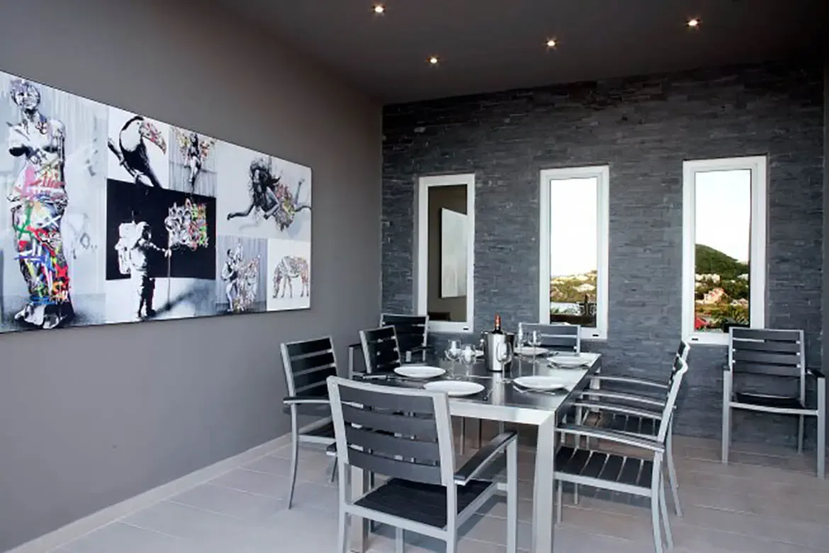 The modern dining area features a large contemporary art mural, dark slate accent wall with three vertical windows showing landscape views, and a dining table set for six.