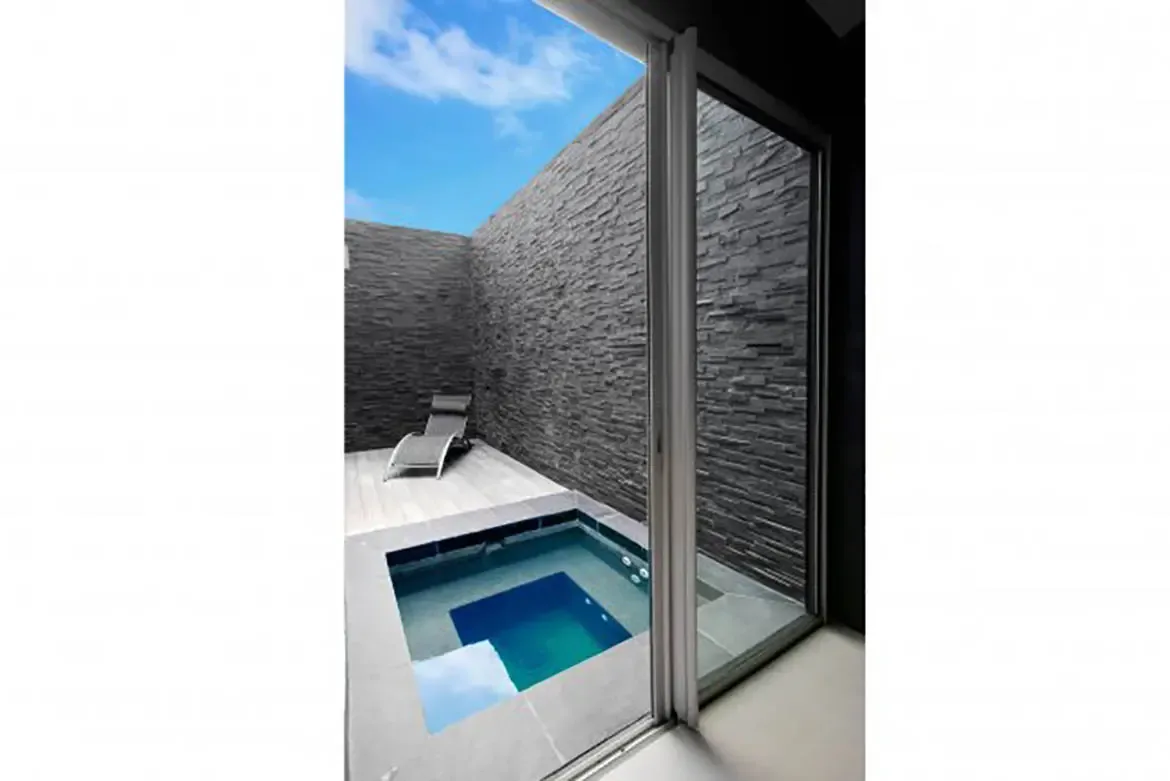 A private outdoor nook features a small plunge pool, lounge chair, and high dark stone walls under open sky.