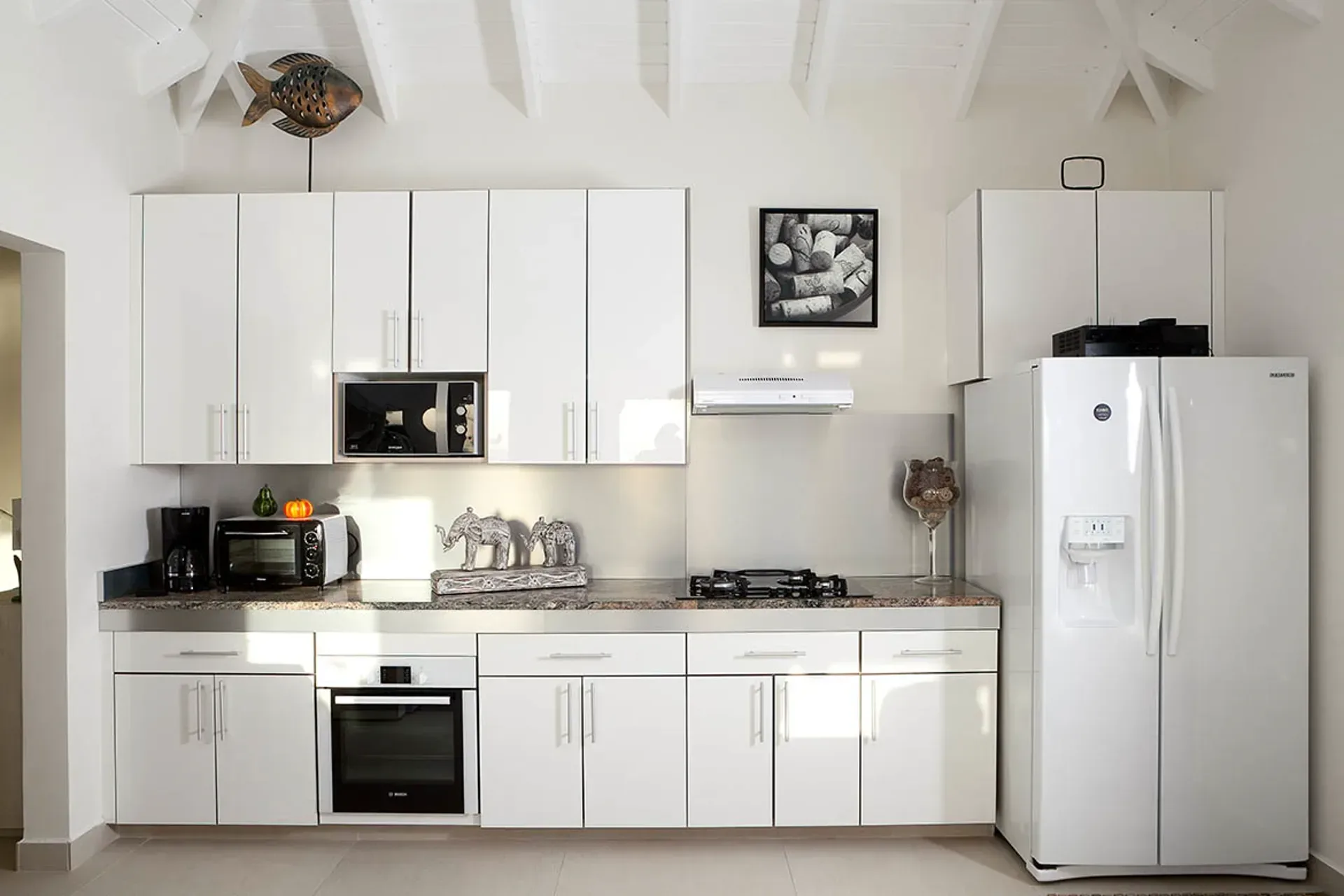 White kitchen with granite counters and vaulted wood ceiling.